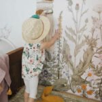 Wandsticker, der grosse bunte Wiese mit verschiedenen Pflanzen und Blumen darstellt und der von einem kleinem Junge bewundert ist
