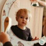 A little boy looking into wooden mirror with a bird design on the wall
