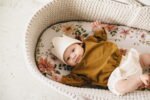 Ein Baby im Moses Korb gekleidet in einer Bluse mit Gänse Stickerei aus Bio-Baumwolle mit GOTs Zertifikat – Karamell