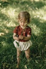Ein Mädchen im Garten gekleidet in Baby Wickelbody aus Bio-Baumwolle mit GOTs Zertifikat und kurzen Ärmel mit Gänse Muster