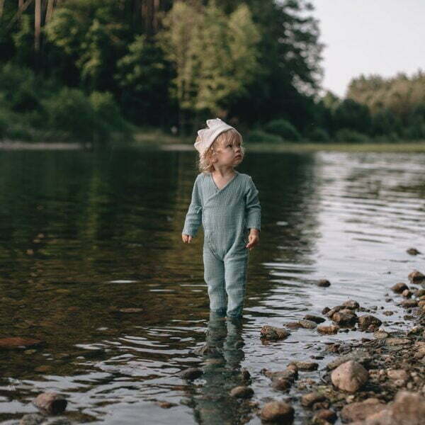 A girl at the lake wearing a baby wrap jumpsuit made of organic muslin with GOTs certificate