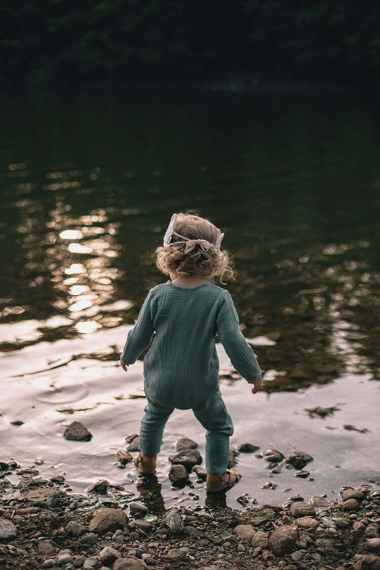 Ein Mädchen am See gekleidet in Baby Overall aus Bio-Musselin mit GOTs Zertifikat
