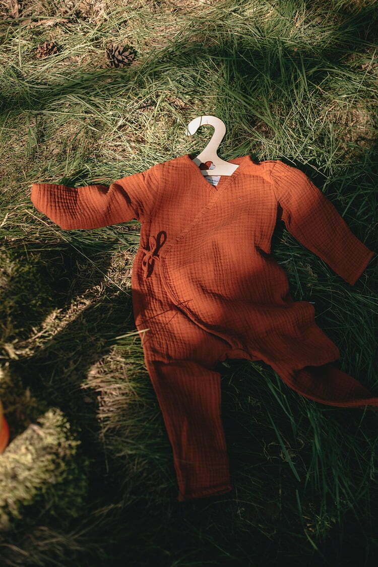 Baby Overall auf dem Grass aus Musselin Bio Baumwolle in rotbrauner Farbe