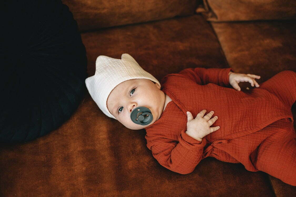 A baby gekleidet in einem Overall aus Musselin Bio Baumwolle in rotbrauner Farbe