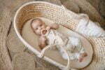 Ein Baby im Moses Korb gekleidet in ein Boho Wickelbody und Leggings aus Bio-Baumwoll
