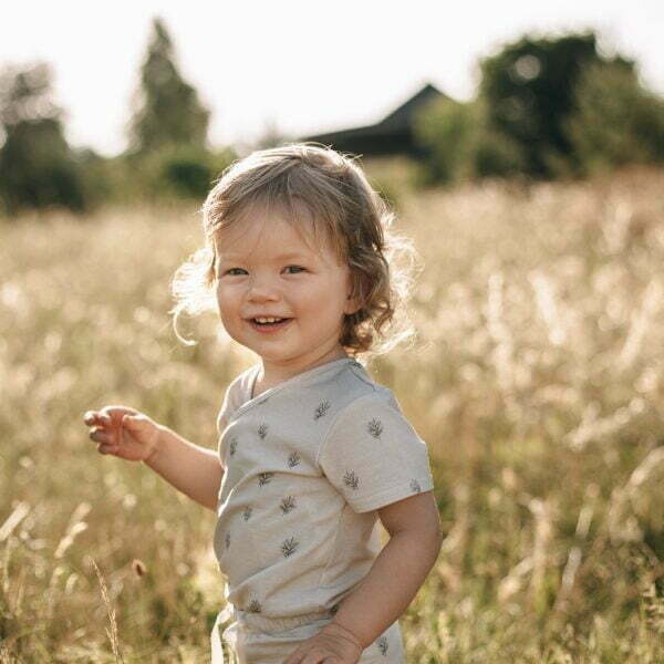 A girl on the meadow wearing a wrapover bodysuit with short sleeves and Boho Leaf design made of organic cotton