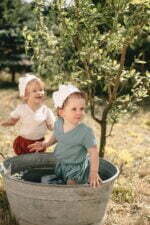 Kinder im Garten angezogen in einem Set von Wickelhemd und Bloomers aus zertifiziertem Bio-Musselin