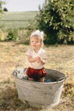 ein Mädchen im Garten gekleidet in Baby Wickelhemd und bloomers aus Bio Musselin mit GOTs Zertifikat